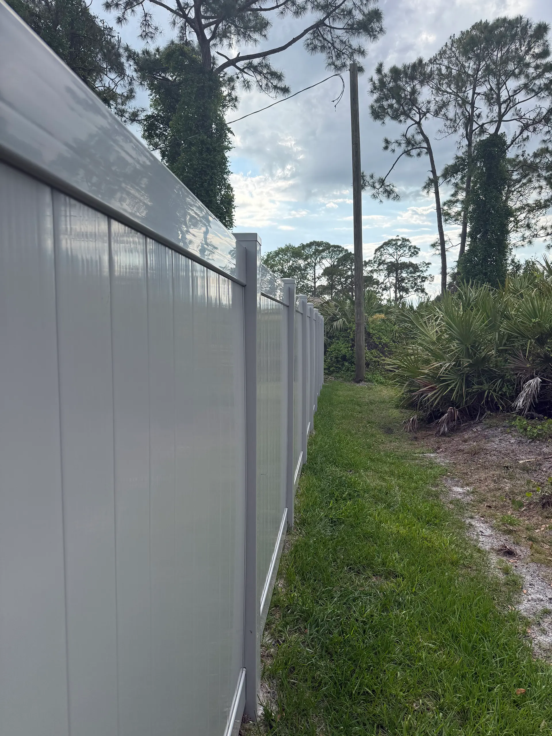 Tall white vinyl privacy fence along a Florida tree line